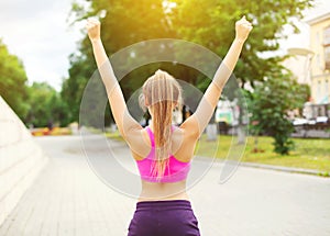 Fitness happy runner woman enjoying after training in city park, runner winner, raises hands up, sport and healthy lifestyle