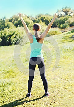 Fitness happy runner woman enjoying after training in park, runner winner, raises hands up, sport and healthy lifestyle