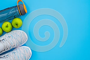 Fitness and healthy active lifestyle background concept.  Training sneakers,  water bottle and green apples on blue table
