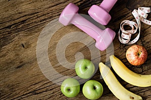 Fitness, healthy and active lifestyles Concept, dumbbells, measuring tape, bananas and apples on wood background. Top view with c