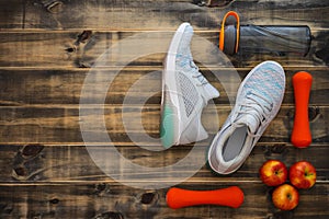 Fitness, healthy and active lifestyles love concept, dumbbells, sport shoes, bottle of waters and apples on wood background. Top