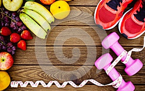 Fitness, healthy fruits, diet and active lifestyles Concept, dumbbells, tape measure, sport shoes, fresh fruits on wood