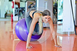 Fitness, home and diet concept - smiling girl exercising with fitness ball at gym