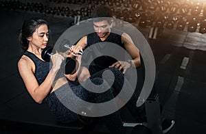 Fitness instructor exercising with his client at the gym, Personal trainer helping woman working with heavy dumbbells