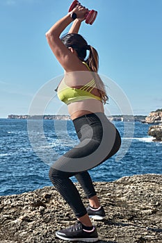 FITNESS LATIN WOMAN IN SPORTS SET TRAINING WITH ELASTIC BAND, WEIGHTS, GYM EXERCISES, IN FRONT OF THE WATER