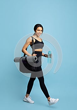 Fitness lifestyle concept. Excited african american lady going to gym, carrying bag and water bottle on blue background