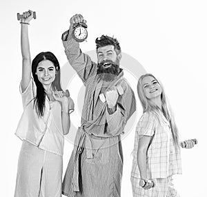 Fitness lifestyle concept. Trainer, macho with attractive girls do morning exercises. Bearded man holds alarm clock