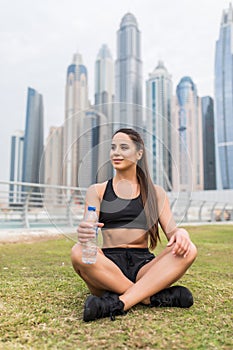 Fitness and lifestyle concept. Young woman drinking water after doing sports outdoors in front of skyscrapers