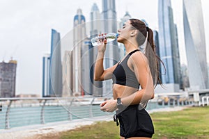 Fitness and lifestyle concept. Young woman drinking water after doing sports outdoors in front of skyscrapers