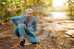 Fitness lifestyle portrait of young attractive Asian runner woman suffering sport injury during jogging workout on sunset road