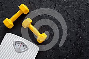 Fitness for losing weight. Bathroom scale and dumbbell on black background top view