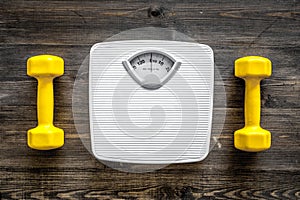 Fitness for losing weight. Bathroom scale and dumbbell on wooden background top view