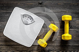 Fitness for losing weight. Bathroom scale and dumbbell on wooden background top view