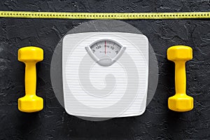 Fitness for losing weight. Bathroom scale, measuring tape and dumbbell on black background top view