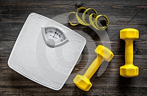 Fitness for losing weight. Bathroom scale, measuring tape and dumbbell on wooden background top view