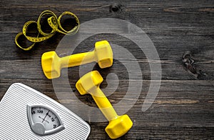 Fitness for losing weight. Bathroom scale, measuring tape and dumbbell on wooden background top view copyspace