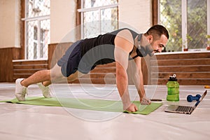 Fitness man in black sports wear doing up push ups exercise in empty gym or home watching online sports videos. Muscular