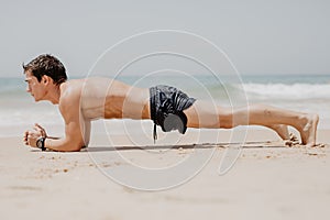 Fitness man doing push-up exercise on beach. Portrait of fit guy working out his arm muscles and body core with pushup exercises o photo