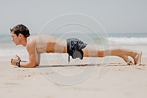 Fitness man doing push-up exercise on beach. Portrait of fit guy working out his arm muscles and body core with pushup exercises o