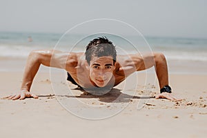 Fitness man doing push-up exercise on beach. Portrait of fit guy working out his arm muscles and body core with pushup exercises o