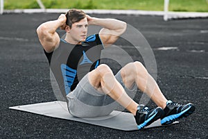 Fitness man doing sit ups in the stadium, working out. Active male exercising abdominals