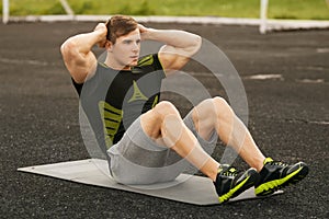 Fitness man doing sit ups in the stadium working out. Muscular male exercising abdominals, outdoor
