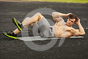 Fitness man doing sit ups in the stadium working out. Muscular male exercising abdominals, outdoor