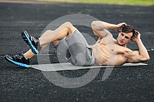 Fitness man doing sit ups in the stadium working out. Muscular male exercising abdominals, outdoor