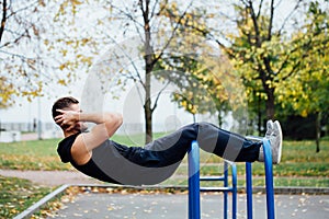 Fitness man doing stomach workouts on horizontal bar outdoors