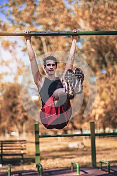 Fitness man doing workouts on horizontal bar outdoors