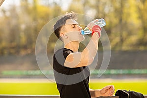 Fitness man drinking water from bottle. Thirsty athlete having cold refreshment drink after intense exercise