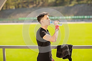 Fitness man drinking water from bottle. Thirsty athlete having cold refreshment drink after intense exercise