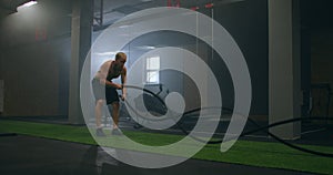 Fitness man exercising with battle rope abandoned warehouse. Tough man working out in cross training gym made inside old