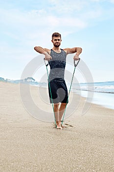 Fitness Man Exercising At Beach, Doing Expander Exercise Outdoor