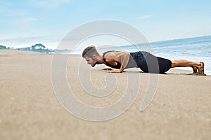 Fitness Man Exercising, Doing Push Ups Exercise On Beach. Sports