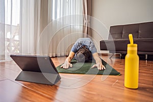 Fitness man exercising on the floor at home and watching fitness videos in a tablet. People do sports online because of