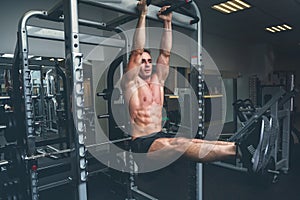 Fitness man hanging on horizontal bar performing legs raises, in the gym