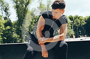 Fitness man resting after running and exercising, listening the music on earphones outdoors. Young muscular male rest after a hard