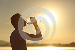 Fitness man silhouette drinking water from a bottle photo