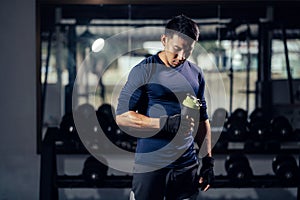 Fitness man in sportswear holding a bottle water or protein shake for drink in fitness gym. Health care and workout. Asian man