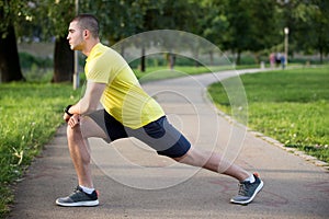 Fitness man stretching arm shoulder before outdoor workout. Sporty male athlete in an urban park warming up.