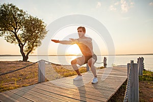 Fitness man training air squat exercise on beach outside. Fit male exercising crossfit outside. Young handsome caucasian