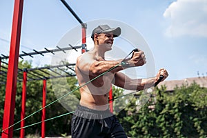 Fitness man training chest with resistance bands at street gym yard. Outdoor workout. Body workout with equipment