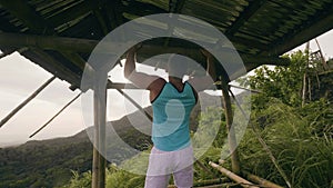 Fitness man training pulling up exercise on horizontal bar in tropical forest. Athlete man doing pull up workout on