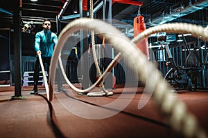 Fitness man working out with battle ropes at gym.