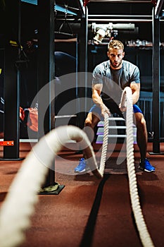 Fitness man working out with battle ropes at gym.