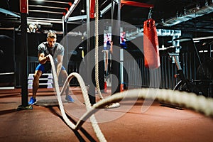 Fitness man working out with battle ropes at gym.