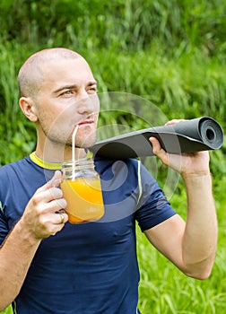 Fitness man with yoga mat holding a glass of orange juice