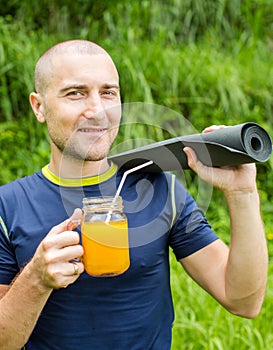 Fitness man with yoga mat holding a glass of orange juice