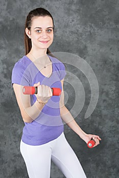 Fitness model woman with dumbbells on grey studio